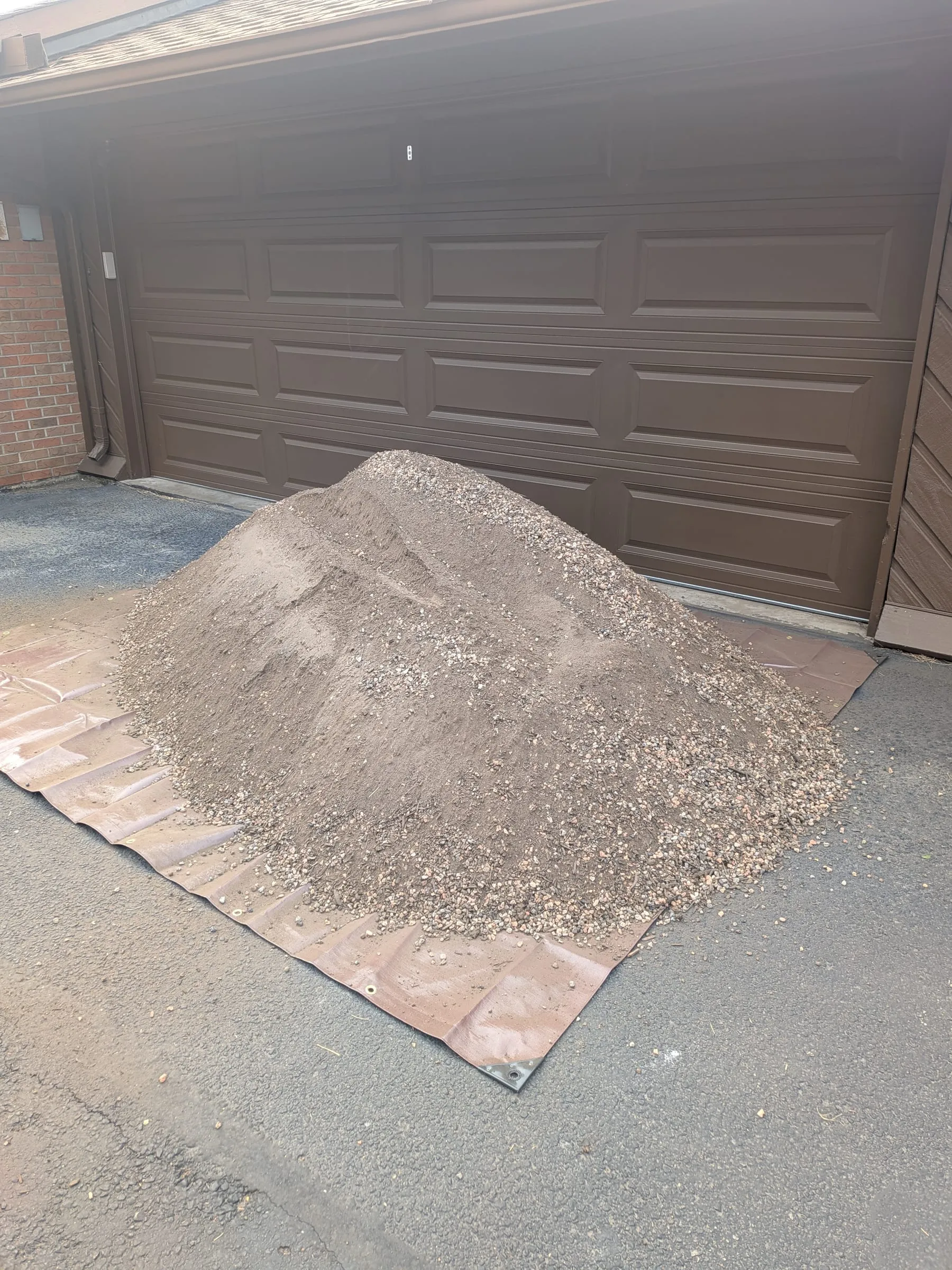 A large pile of soil mix on a tarp in front of a brown garage door